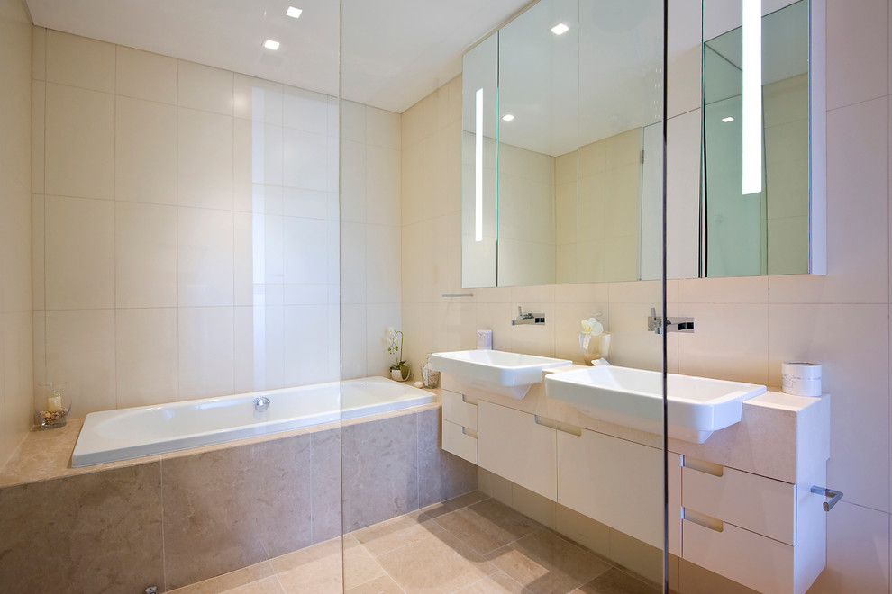 Inspiration for a contemporary bathroom in Other with limestone benchtops, limestone floors, a drop-in sink, glass-front cabinets, beige cabinets, a drop-in tub, a curbless shower, a one-piece toilet, beige tile, stone tile and beige walls.