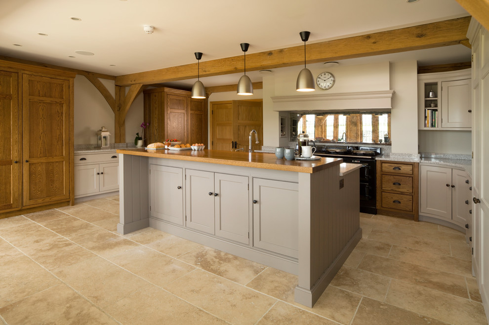 Photo of a mid-sized country kitchen in Hertfordshire with recessed-panel cabinets, grey cabinets, wood benchtops, mirror splashback, with island, beige floor and brown benchtop.