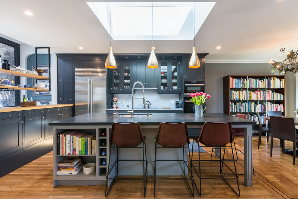 This is an example of a transitional eat-in kitchen in San Francisco with an undermount sink, glass-front cabinets, white splashback, stainless steel appliances, medium hardwood floors, with island and grey cabinets.