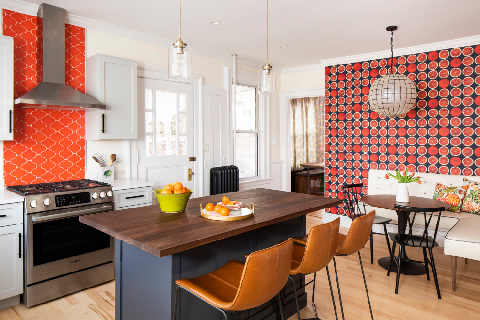 Example of a mid-sized transitional l-shaped light wood floor and beige floor eat-in kitchen design in Boston with white cabinets, orange backsplash, ceramic backsplash, stainless steel appliances, an island, shaker cabinets, wood countertops and brown countertops
