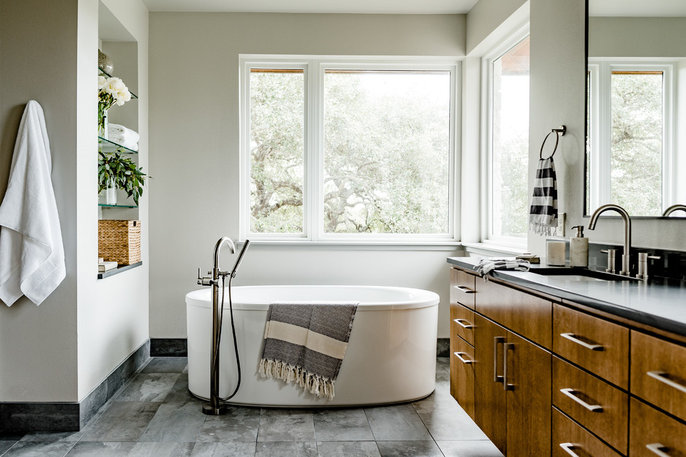 This is an example of a mid-sized contemporary master bathroom in Austin with flat-panel cabinets, brown cabinets, a freestanding tub, black benchtops, white walls, an undermount sink and grey floor.