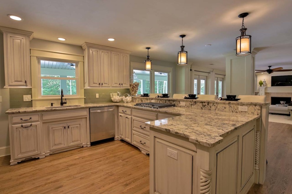 Large contemporary l-shaped open plan kitchen in Atlanta with an undermount sink, raised-panel cabinets, dark wood cabinets, granite benchtops, green splashback, glass tile splashback, stainless steel appliances, light hardwood floors and a peninsula.