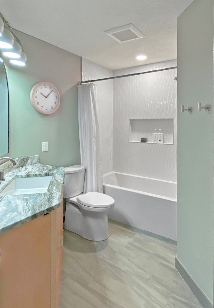 This is an example of a medium sized family bathroom in Minneapolis with flat-panel cabinets, light wood cabinets, an alcove bath, a shower/bath combination, a two-piece toilet, white tiles, ceramic tiles, green walls, ceramic flooring, a submerged sink, quartz worktops, grey floors, a shower curtain, multi-coloured worktops, a wall niche, a single sink and a built in vanity unit.