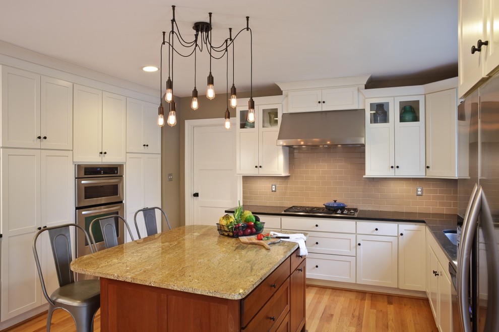 Mid-sized transitional u-shaped light wood floor kitchen photo in Baltimore with white cabinets, beige backsplash, subway tile backsplash, stainless steel appliances and an island