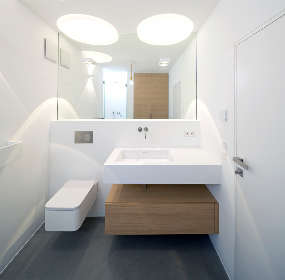 Minimalist powder room photo in Munich with flat-panel cabinets, medium tone wood cabinets, a two-piece toilet, white walls, an integrated sink, solid surface countertops, white countertops and a floating vanity
