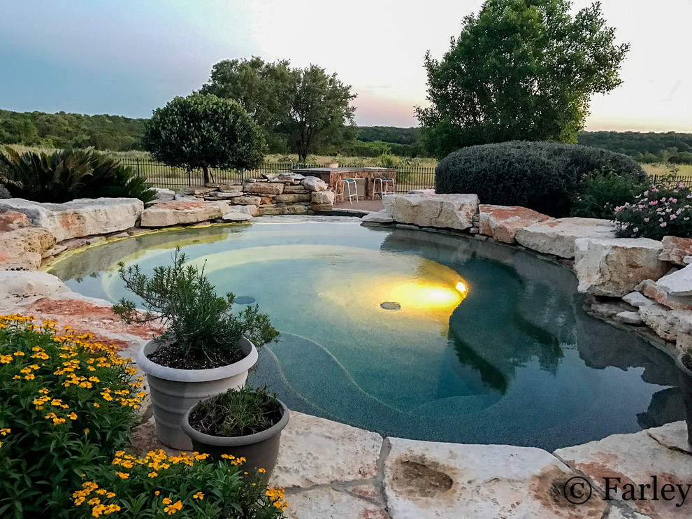 Expansive country backyard custom-shaped natural pool in Dallas with a water feature and natural stone pavers.