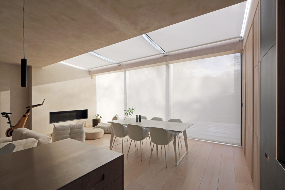 Photo of a large modern kitchen/dining room in London with light hardwood flooring, a ribbon fireplace, a metal fireplace surround, a chimney breast, beige walls and beige floors.