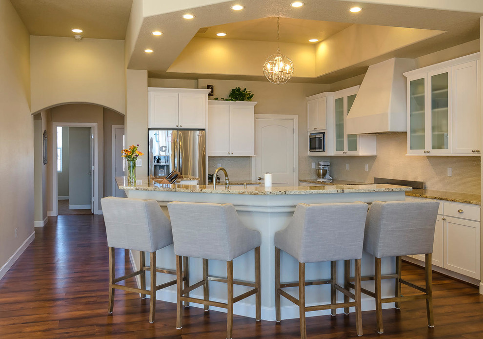 This is an example of a mid-sized l-shaped kitchen pantry in Albuquerque with an undermount sink, shaker cabinets, white cabinets, granite benchtops, beige splashback, glass sheet splashback, stainless steel appliances, with island and dark hardwood floors.