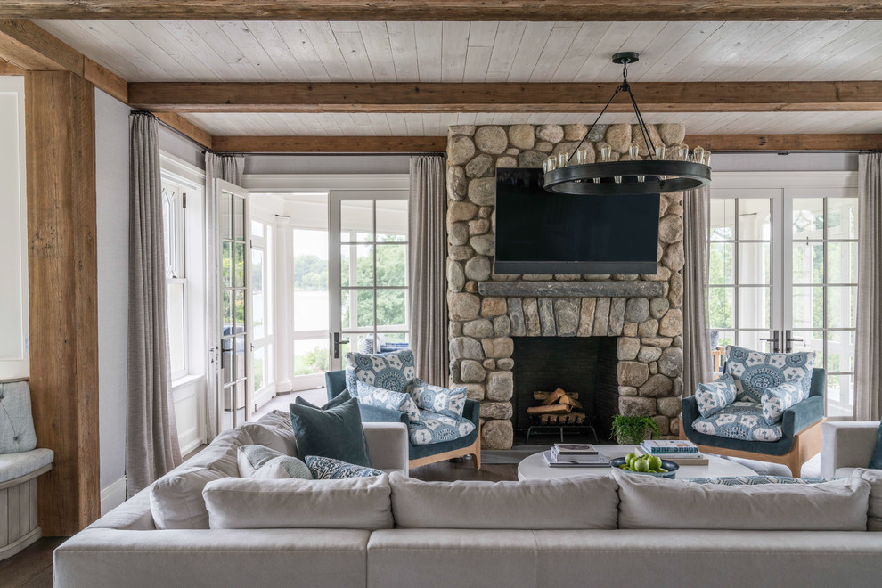 Large beach style open concept family room in Other with grey walls, a standard fireplace, a stone fireplace surround, a wall-mounted tv, medium hardwood floors and brown floor.