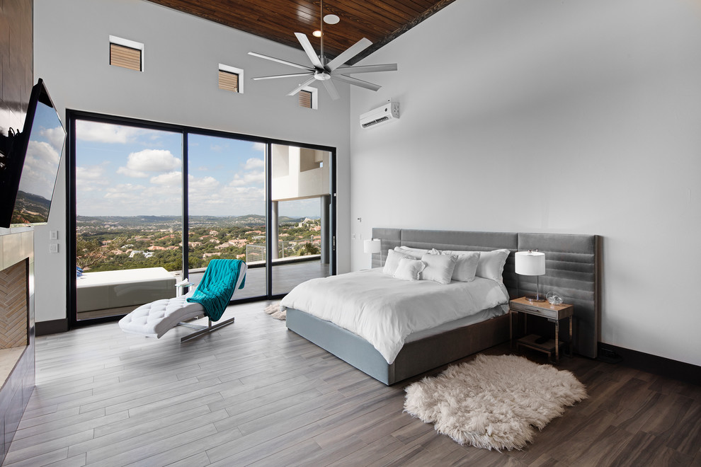 Photo of a large contemporary master bedroom in Austin with white walls, porcelain floors, a tile fireplace surround and a standard fireplace.