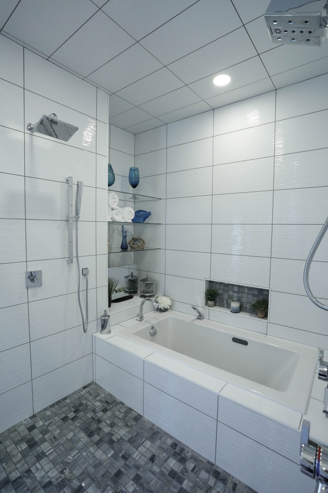 На фото: большая главная ванная комната в стиле модернизм с плоскими фасадами, белыми фасадами, накладной ванной, двойным душем, унитазом-моноблоком, белой плиткой, керамической плиткой, белыми стенами, полом из керамогранита, врезной раковиной, душем с раздвижными дверями, нишей, тумбой под одну раковину и подвесной тумбой с