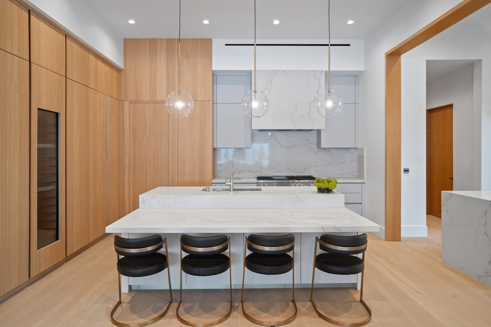 Photo of an expansive modern u-shaped eat-in kitchen in Los Angeles with an undermount sink, flat-panel cabinets, light wood cabinets, solid surface benchtops, white splashback, panelled appliances, light hardwood floors, multiple islands, brown floor and white benchtop.