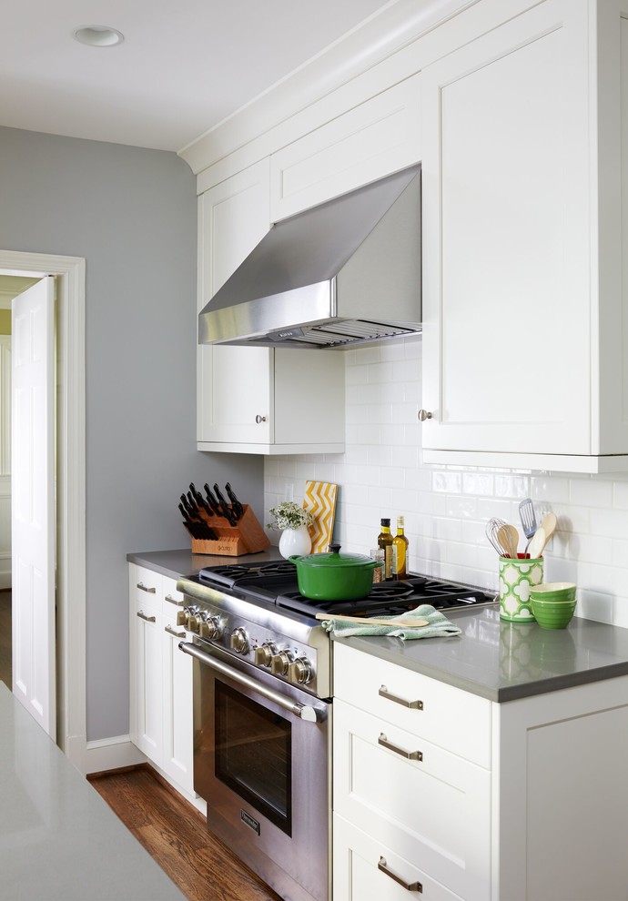 Enclosed kitchen - mid-sized transitional u-shaped dark wood floor and brown floor enclosed kitchen idea in DC Metro with a farmhouse sink, shaker cabinets, white cabinets, solid surface countertops, white backsplash, subway tile backsplash, stainless steel appliances and an island
