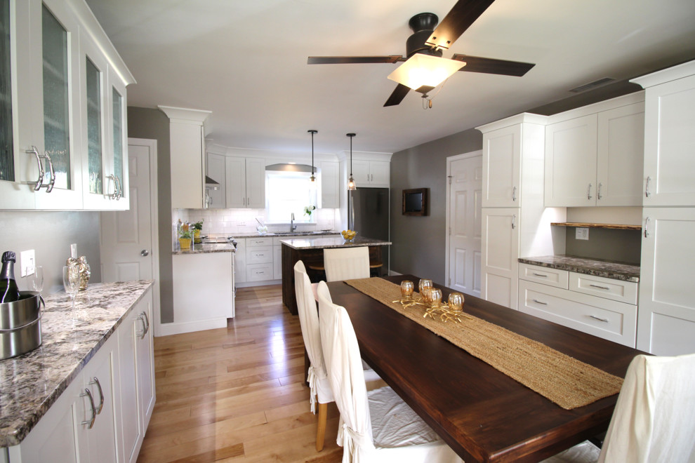 Kitchen/dining room combo - mid-sized transitional l-shaped light wood floor kitchen/dining room combo idea in Burlington with a single-bowl sink, shaker cabinets, white cabinets, granite countertops, white backsplash, ceramic backsplash, stainless steel appliances and an island