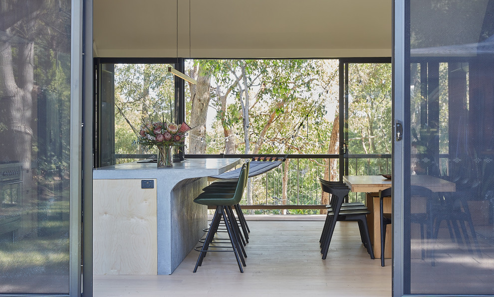 This is an example of a large contemporary galley open plan kitchen in Perth with a double-bowl sink, flat-panel cabinets, light wood cabinets, concrete benchtops, white splashback, porcelain splashback, black appliances, light hardwood floors, with island, beige floor, grey benchtop and vaulted.