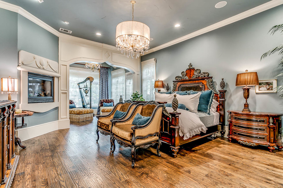 Inspiration for a traditional master bedroom in Dallas with blue walls, medium hardwood floors, a corner fireplace, a plaster fireplace surround and brown floor.