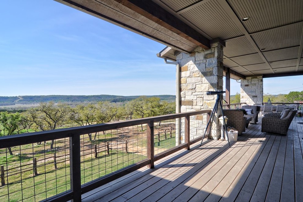 This is an example of an expansive country backyard deck in Austin with a roof extension.