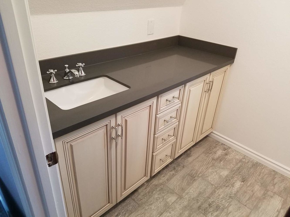 This is an example of a small transitional single-wall wet bar in San Francisco with an undermount sink, raised-panel cabinets, white cabinets, solid surface benchtops, light hardwood floors, beige floor and grey benchtop.