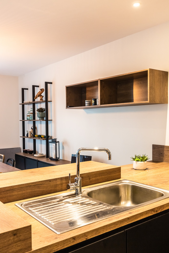This is an example of a mid-sized modern u-shaped open plan kitchen in Other with a drop-in sink, wood benchtops, brown splashback, timber splashback, panelled appliances, no island, grey floor and brown benchtop.