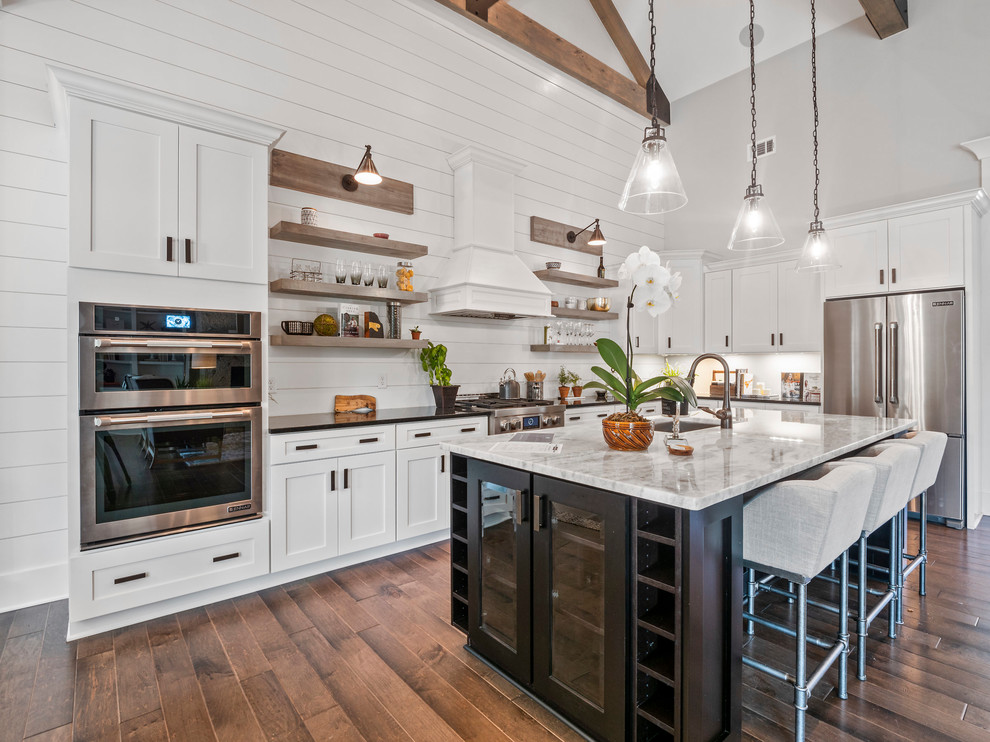 Design ideas for a country l-shaped kitchen in Atlanta with an undermount sink, shaker cabinets, white cabinets, stainless steel appliances, dark hardwood floors, with island, brown floor and black benchtop.