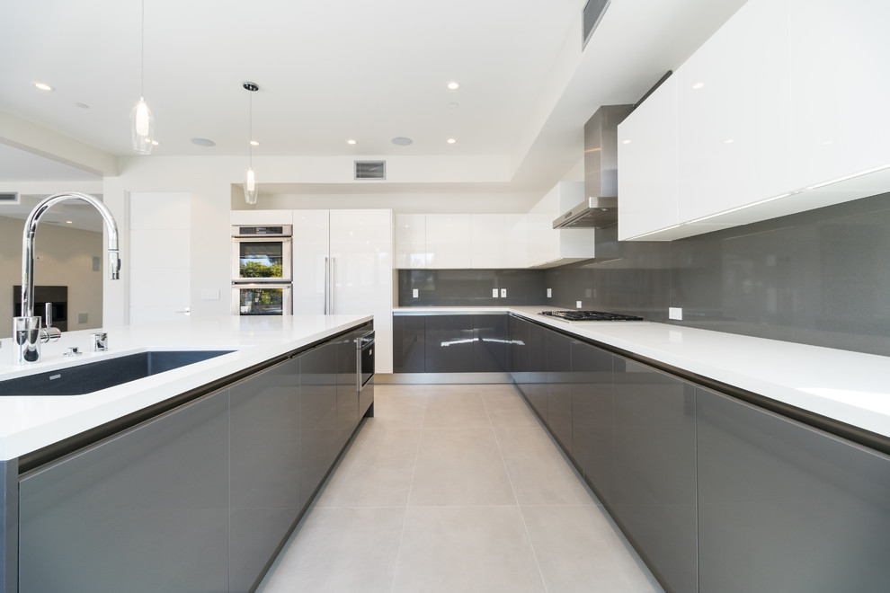 This is an example of a large contemporary u-shaped kitchen in Los Angeles with an undermount sink, flat-panel cabinets, grey cabinets, quartzite benchtops, grey splashback, stone slab splashback, stainless steel appliances, porcelain floors, with island, grey floor and white benchtop.