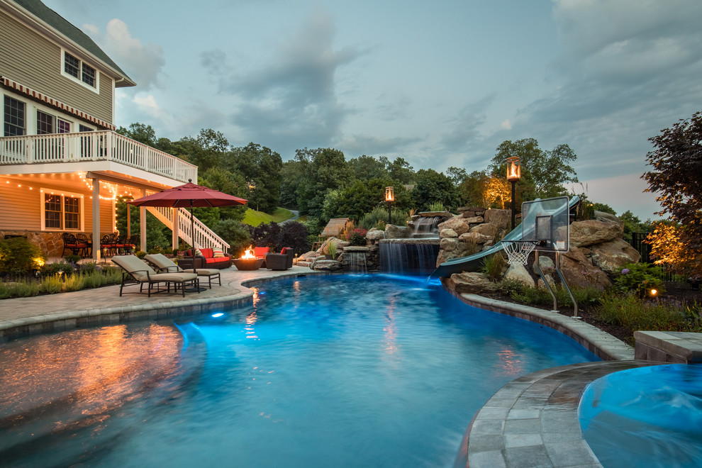 This is an example of a mid-sized country backyard custom-shaped pool in New York with a water slide and brick pavers.