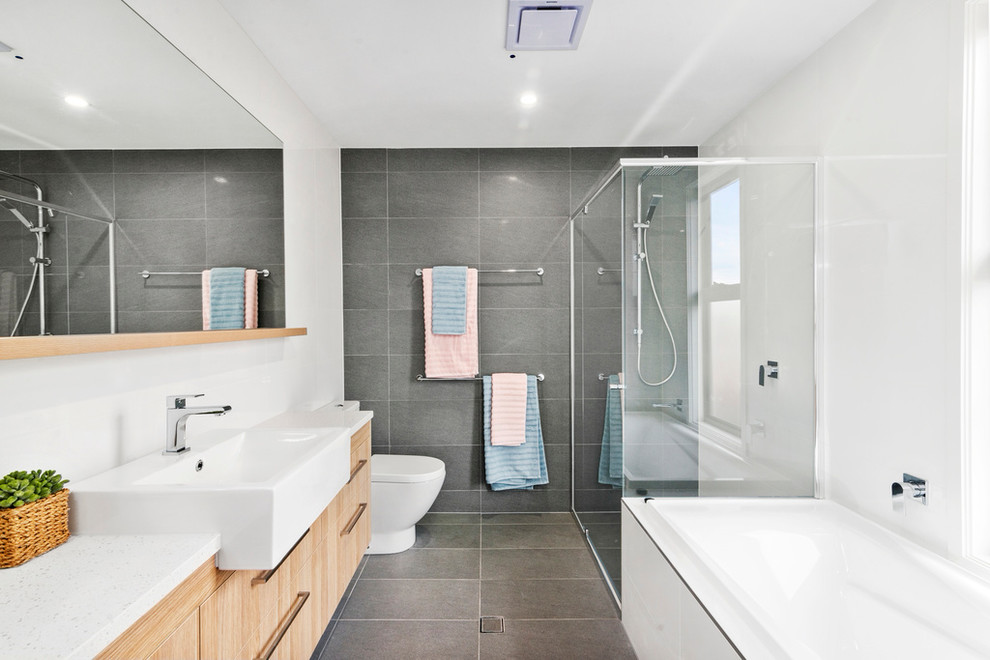 Design ideas for a contemporary bathroom in Gold Coast - Tweed with flat-panel cabinets, medium wood cabinets, a drop-in tub, a corner shower, gray tile, white walls, a drop-in sink, grey floor, a sliding shower screen and white benchtops.