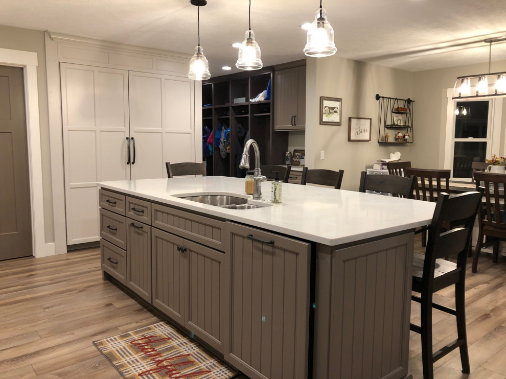 Expansive transitional u-shaped open plan kitchen in Grand Rapids with an undermount sink, recessed-panel cabinets, white cabinets, quartz benchtops, multi-coloured splashback, ceramic splashback, stainless steel appliances, vinyl floors, with island, brown floor and white benchtop.