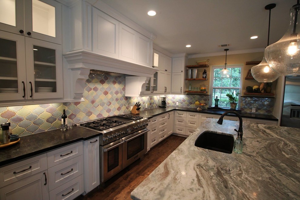 Example of a large minimalist u-shaped medium tone wood floor, vaulted ceiling and brown floor eat-in kitchen design in Houston with an island, an undermount sink, white cabinets, multicolored backsplash, ceramic backsplash, stainless steel appliances, multicolored countertops and shaker cabinets