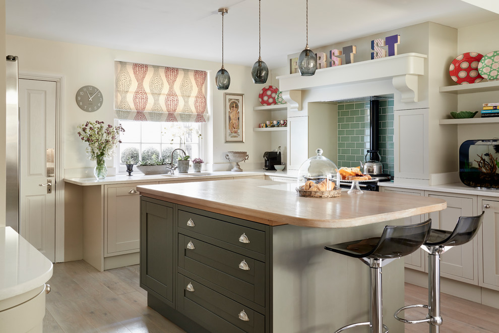 This is an example of a mid-sized eclectic l-shaped kitchen in London with shaker cabinets, grey cabinets, black appliances, light hardwood floors, with island, a double-bowl sink, green splashback, subway tile splashback and white benchtop.