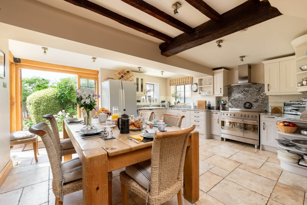 This is an example of a country l-shaped eat-in kitchen in West Midlands with shaker cabinets, white cabinets, white splashback, stainless steel appliances, beige floor and grey benchtop.