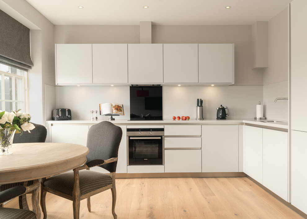 Inspiration for a contemporary l-shaped eat-in kitchen in Edinburgh with an undermount sink, flat-panel cabinets, black splashback, stainless steel appliances, light hardwood floors and no island.