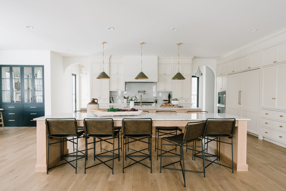 Inspiration for a large transitional galley eat-in kitchen in Salt Lake City with a farmhouse sink, beaded inset cabinets, light wood cabinets, marble benchtops, white splashback, marble splashback, panelled appliances, light hardwood floors, multiple islands, brown floor and white benchtop.