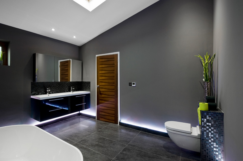 Design ideas for a large contemporary kids bathroom in West Midlands with black cabinets, a freestanding tub, an open shower, a wall-mount toilet, black tile, grey walls, porcelain floors, a drop-in sink, black floor, an open shower and white benchtops.