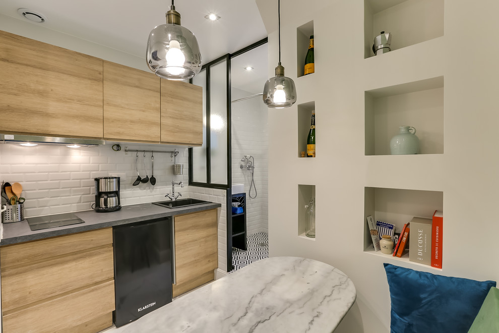This is an example of a small midcentury single-wall open plan kitchen in Paris with an undermount sink, flat-panel cabinets, light wood cabinets, laminate benchtops, white splashback, porcelain splashback, black appliances, ceramic floors, no island, white floor and grey benchtop.