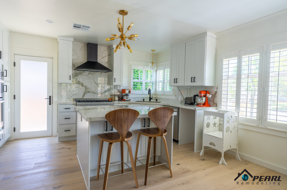 This is an example of a mid-sized modern l-shaped eat-in kitchen in Los Angeles with a drop-in sink, shaker cabinets, white cabinets, marble benchtops, white splashback, marble splashback, stainless steel appliances, light hardwood floors, with island, beige floor and white benchtop.
