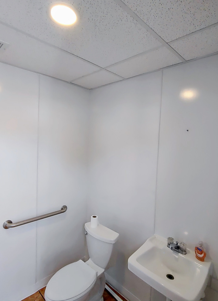Klassisk inredning av ett litet badrum med dusch, med en toalettstol med separat cisternkåpa, vita väggar, klinkergolv i keramik, ett väggmonterat handfat och brunt golv