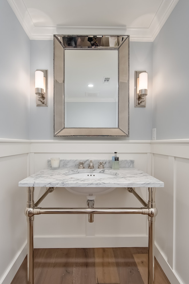 Inspiration for a small beach style powder room in Orange County with recessed-panel cabinets, white cabinets, grey walls, light hardwood floors, an undermount sink and marble benchtops.