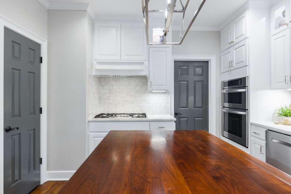 Photo of an expansive traditional l-shaped kitchen/diner in Atlanta with a submerged sink, raised-panel cabinets, white cabinets, engineered stone countertops, white splashback, ceramic splashback, stainless steel appliances, medium hardwood flooring, an island, brown floors and white worktops.