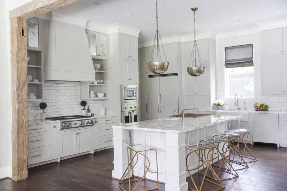 Transitional u-shaped separate kitchen in Houston with a farmhouse sink, shaker cabinets, white cabinets, marble benchtops, white splashback, subway tile splashback, panelled appliances, medium hardwood floors, with island, brown floor and multi-coloured benchtop.