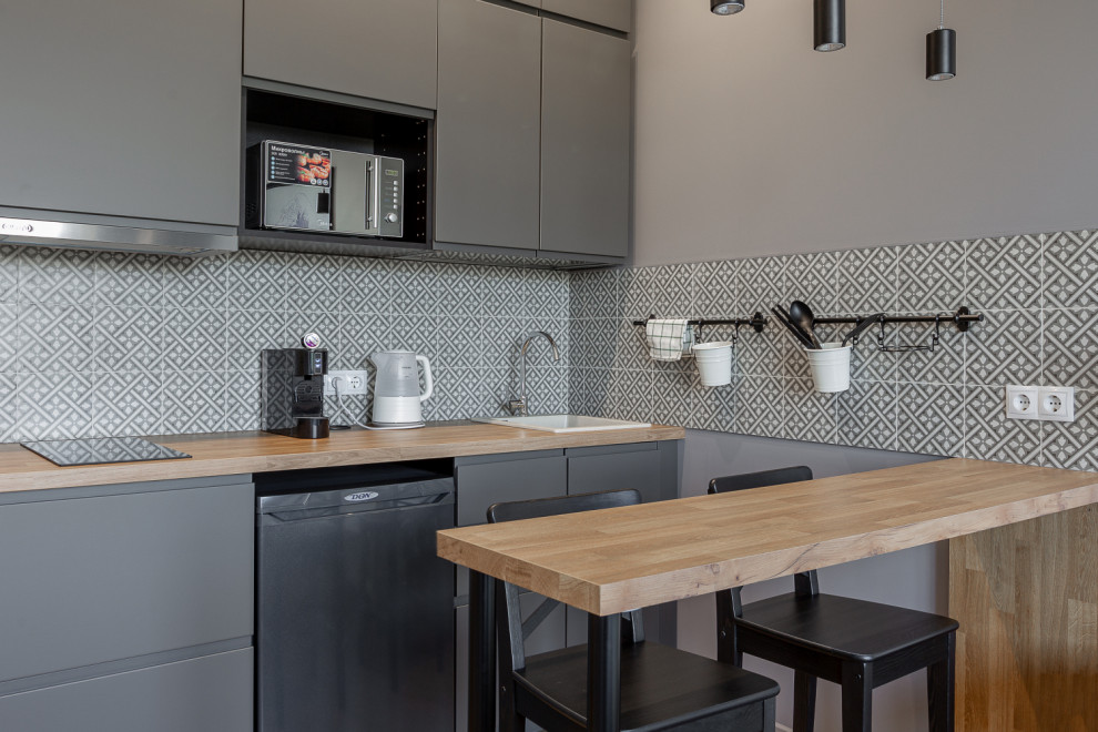 Photo of a small contemporary single-wall open plan kitchen in Moscow with an undermount sink, flat-panel cabinets, grey cabinets, laminate benchtops, black splashback, ceramic splashback, black appliances, laminate floors, brown floor and brown benchtop.