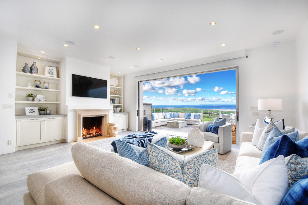 Large beach style open concept family room in Orange County with white walls, light hardwood floors, a standard fireplace, a wall-mounted tv, grey floor and a stone fireplace surround.
