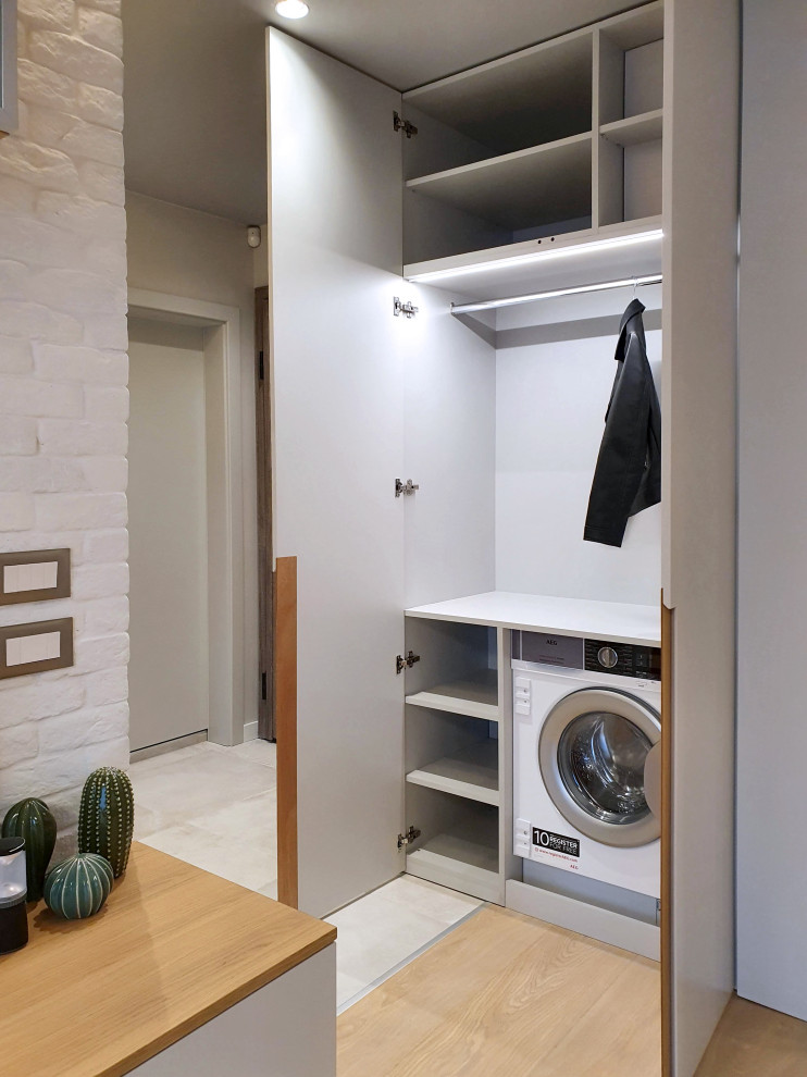 Photo of a small contemporary single-wall laundry cupboard in Other with flat-panel cabinets, grey cabinets, grey walls, light hardwood flooring, an integrated washer and dryer and beige floors.