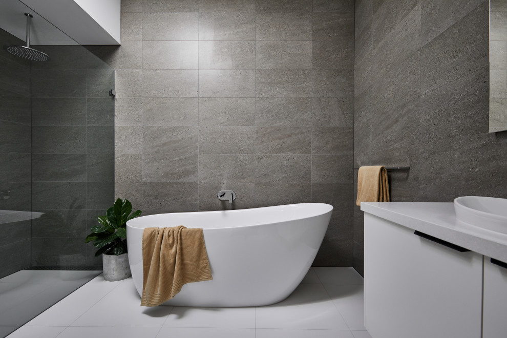 Idée de décoration pour une grande salle de bain design avec des portes de placard blanches, une baignoire indépendante, un carrelage gris, un mur gris, un sol blanc, aucune cabine, un plan de toilette blanc et meuble simple vasque.