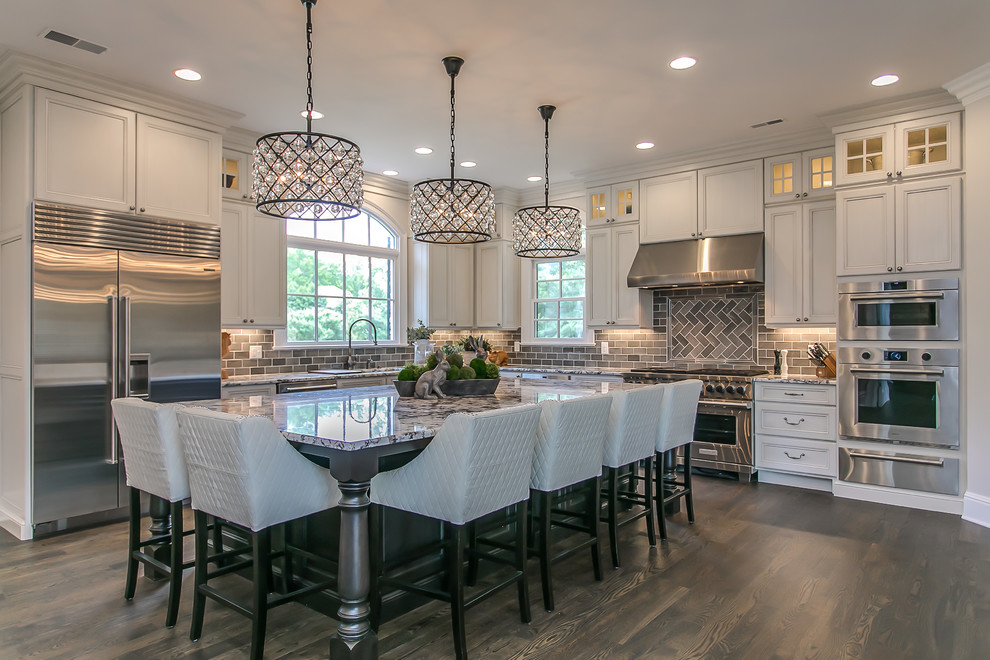 Photo of a large traditional eat-in kitchen in Nashville with flat-panel cabinets, white cabinets, granite benchtops, grey splashback, glass tile splashback, stainless steel appliances, dark hardwood floors, with island, brown floor and multi-coloured benchtop.