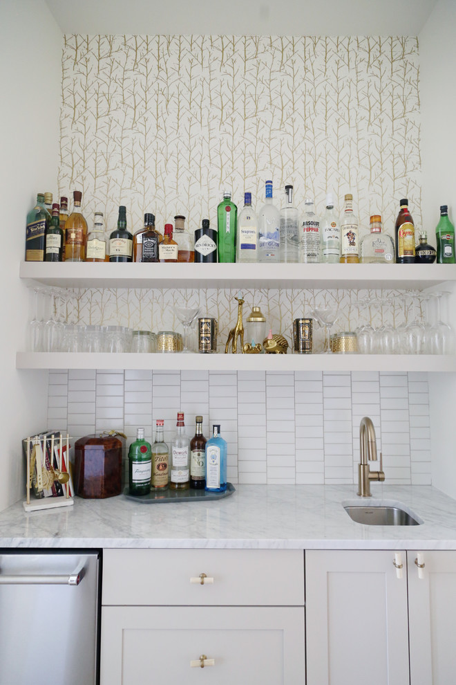 Mid-sized contemporary single-wall wet bar in Other with an undermount sink, shaker cabinets, white cabinets, marble benchtops, white splashback, porcelain splashback and light hardwood floors.