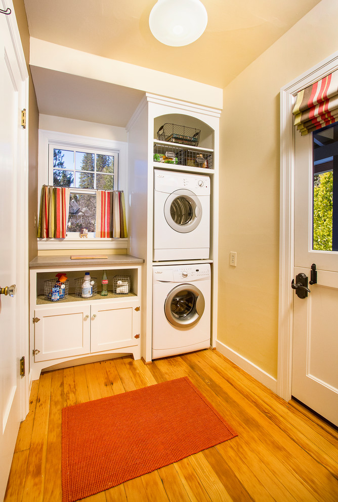 Inspiration for a mid-sized traditional single-wall dedicated laundry room in Sacramento with white cabinets, quartz benchtops, beige walls, light hardwood floors, a stacked washer and dryer, beige floor and beige benchtop.