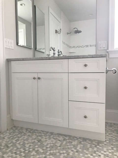 Inspiration for a mid-sized beach style 3/4 bathroom in Philadelphia with recessed-panel cabinets, white cabinets, a drop-in tub, a shower/bathtub combo, a one-piece toilet, white tile, glass tile, grey walls, ceramic floors, an undermount sink and marble benchtops.