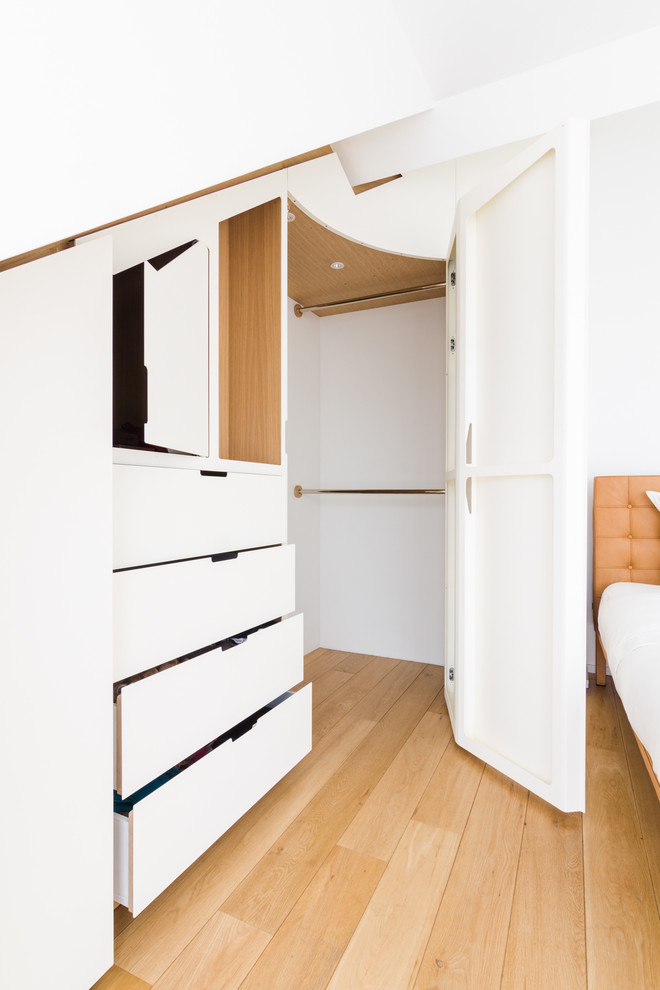 Large contemporary gender-neutral built-in wardrobe in Paris with beaded inset cabinets, white cabinets, light hardwood floors and beige floor.