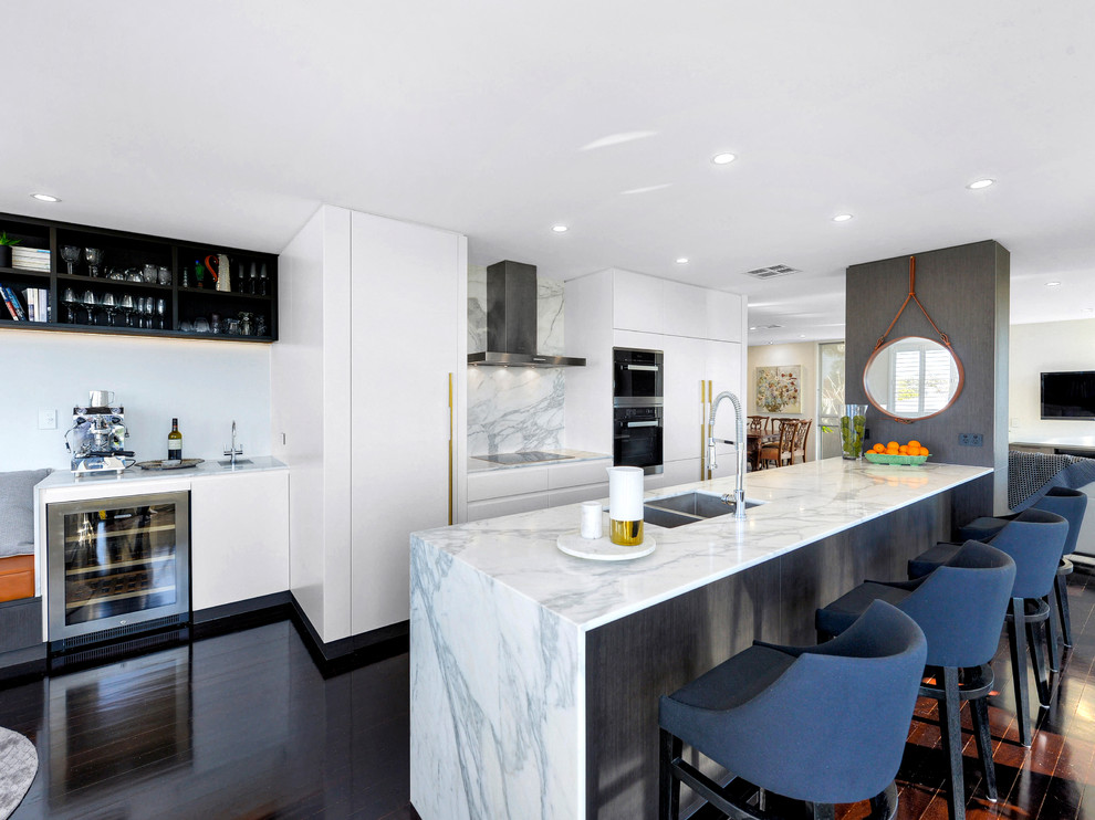 This is an example of a contemporary kitchen in Brisbane with a double-bowl sink, flat-panel cabinets, white cabinets, marble benchtops, white splashback, marble splashback, black appliances, a peninsula and black floor.